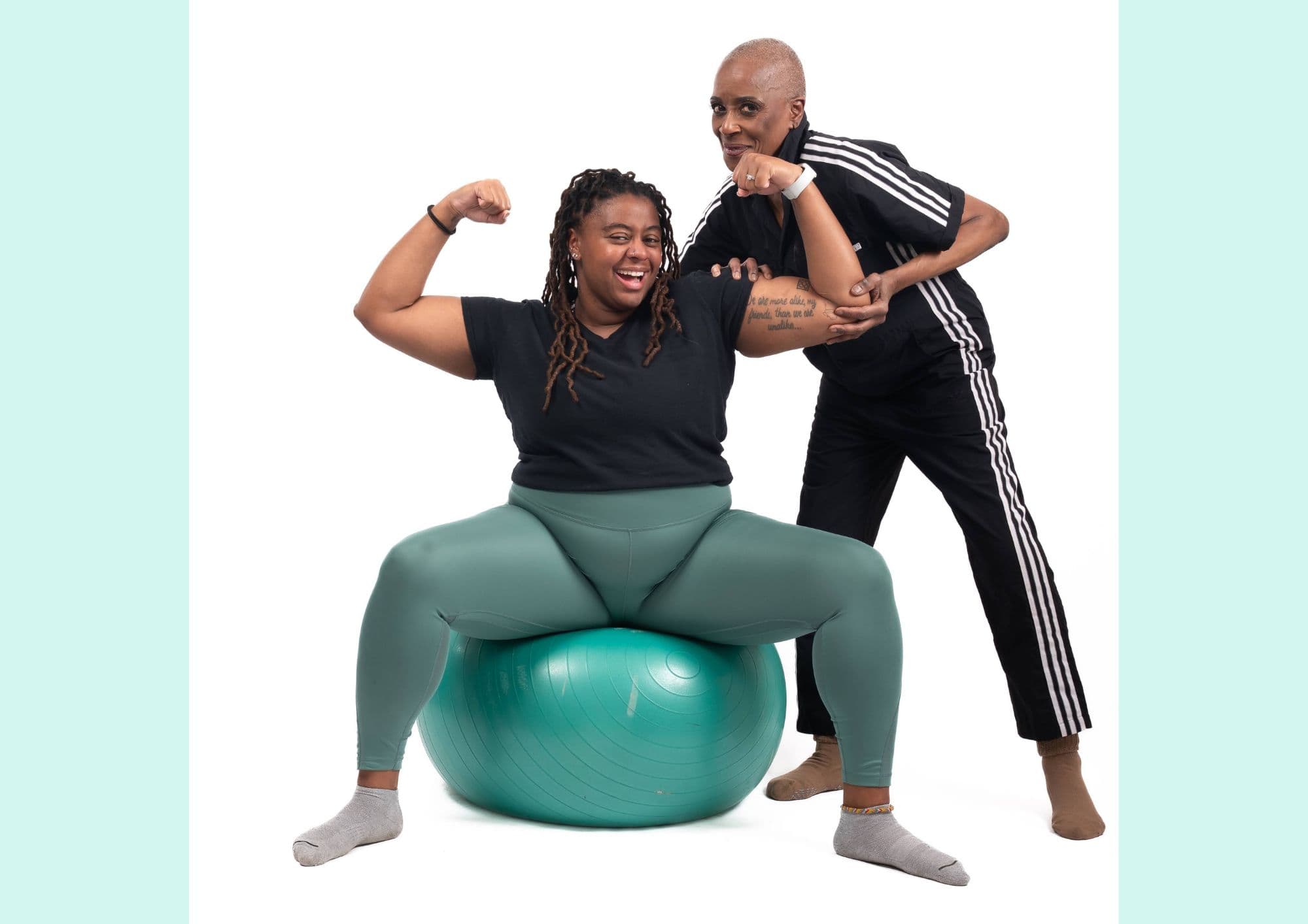 A woman flexes on an exercise ball beside a flexing partner.