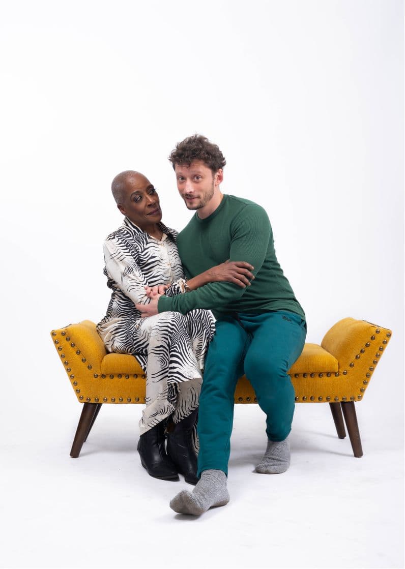 Rhonda and Ben sit close together on a mustard-yellow bench.