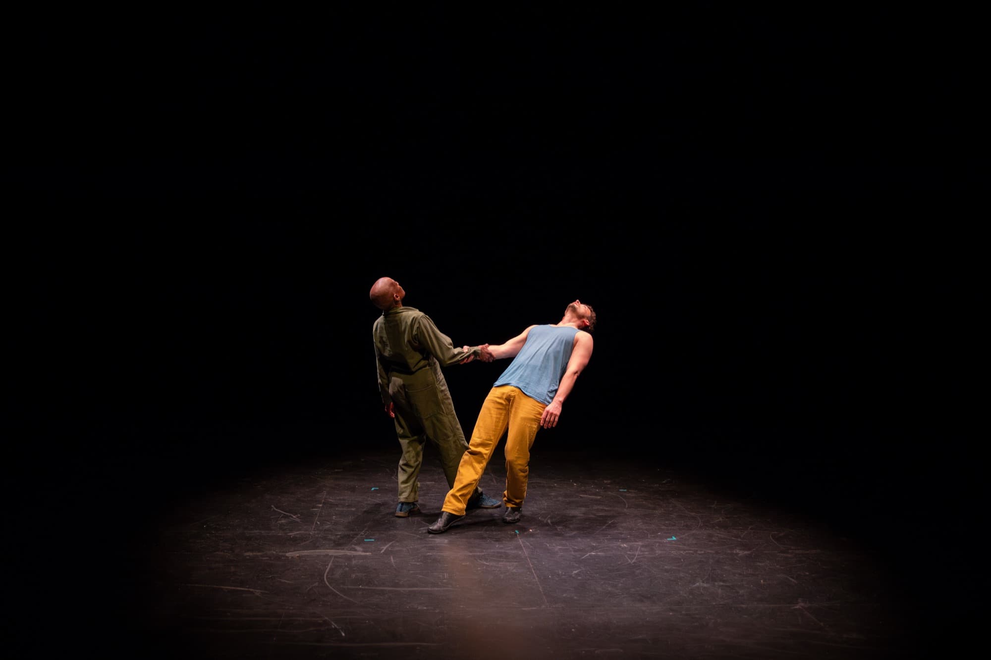 On a dark stage, Rhonda and Ben lean away from each other, holding hands.